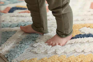 Baby standing on soft colorful carpet, closeup