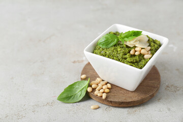 Bowl with delicious pesto sauce, cheese, pine nuts and basil leaves on light table, closeup. Space...