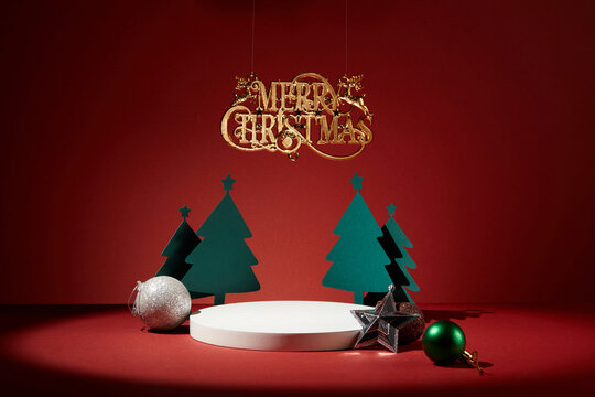 White podium with empty space surrounded by some paper christmas trees, colorful baubles and a silver star. Merry christmas ornament. Holiday illumination and decoration concept