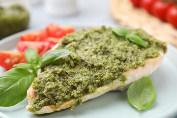 Delicious chicken breast with pesto sauce and basil on table, closeup
