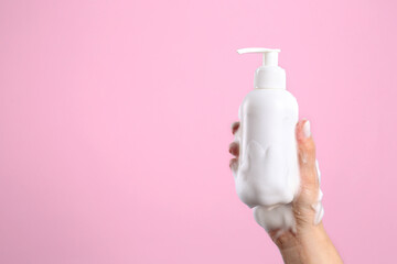Woman with foam on hand holding bottle of skin cleanser against pink background, closeup and space...