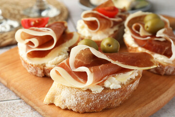 Tasty sandwiches with cured ham, tomatoes and olives on wooden board, closeup