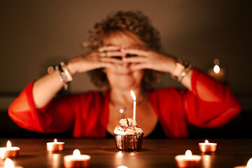 middle aged woman with red sweater, waiting for her birthday surprise, blowing out the candles on the cake, birthday cupcake