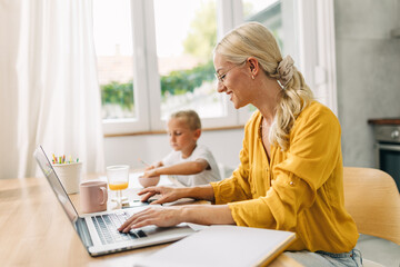 Side view of a businesswoman working on laptop with her child sitting next to her.