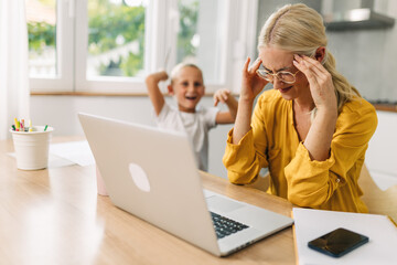 Stressful mother is trying to concentrate on work while her noisy kid is messing around.