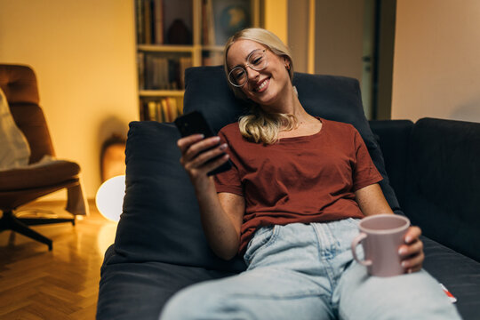 Beautiful smiling woman at home sitting and chatting using smartphone.