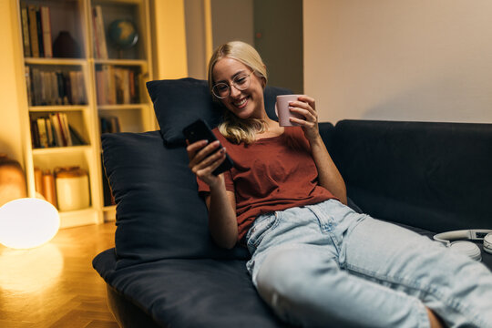 Pretty Caucasian woman resting on the sofa and using a smartphone