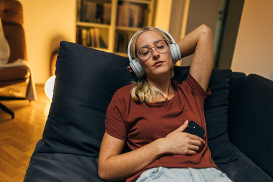 Front view of a woman with closed eyes enjoying listening to music with headphones at home.
