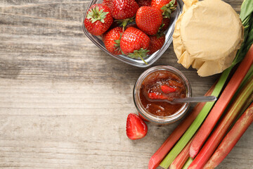 Tasty rhubarb jam, stems and strawberries on wooden table, flat lay. Space for text