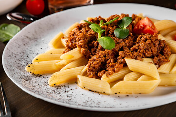 Pasta penne bolognese in white plate on wooden table background