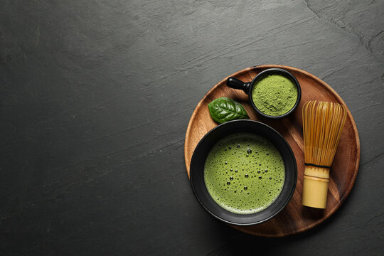 Cup of fresh matcha tea, bamboo whisk and green powder on black table, top view. Space for text
