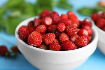 Fresh wild strawberries in bowl on light blue table, closeup