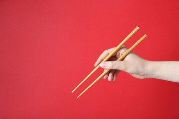 Woman holding pair of wooden chopsticks on red background, closeup. Space for text