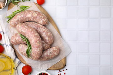 Raw homemade sausages and different products on white tiled table, flat lay. Space for text