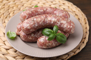Raw homemade sausages and basil leaves on table, closeup