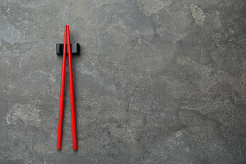 Pair of red chopsticks with rest on grey table, top view. Space for text
