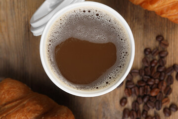 Coffee to go. Paper cup with tasty drink, pastry and beans on wooden table, flat lay