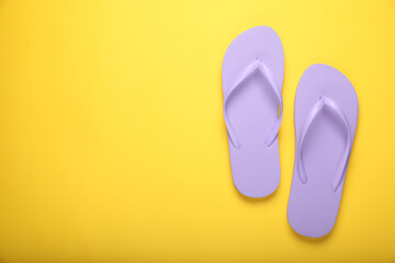 Stylish violet flip flops on yellow background, top view. Space for text