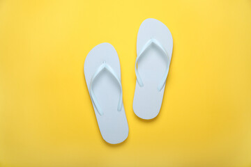 Stylish white flip flops on yellow background, top view