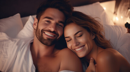 A portrait of a happy young couple who relax in a cozy bed, looking at the camera, smiles fun