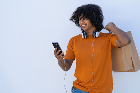 young latin man using cell phone with headphones and shopping bags