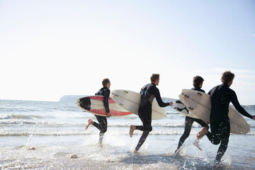 Back view of surfers running in the sea holding surfboards