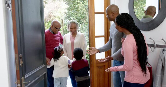 Happy african american parents, son and daughter welcoming grandparents at front door, slow motion