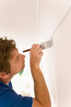 Close up of man painting under ceiling molding with a paint brush
