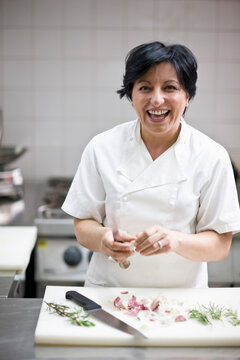 Woman chef peeling garlic with a knife and smiling
