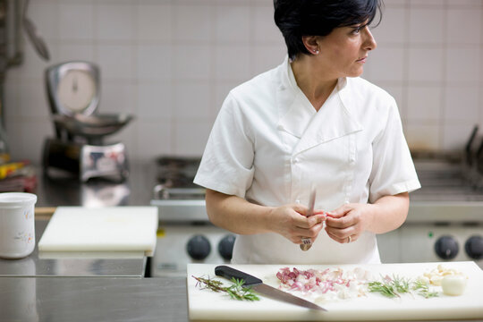 Woman chef peeling garlic with a knife looking to one side
