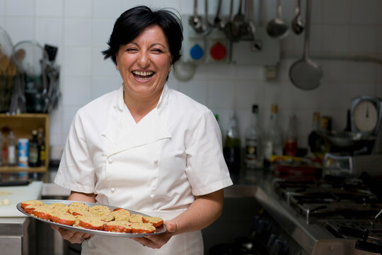 Woman chef holding a tray of stuffed tomatoes and smiling
