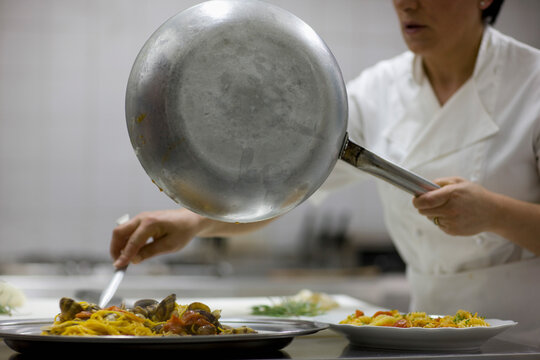 Woman chef holding a frying pan and preparing seafood pasta for service
