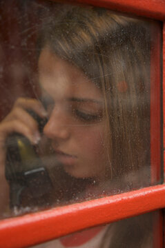 Teenaged girl talking on the telephone inside a London phone booth
