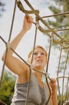 Young woman at obstacle course climbing a cargo net
