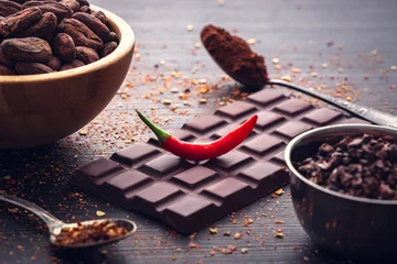 Tuinposter Dark chocolate bar, red hot chilli pepper cayenne,  dry hot chili spices, cocoa beans nibs powder, food tasty design on black wooden background © ValentinValkov