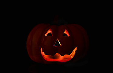The dim light of a Halloween pumpkin illuminates the darkness, creating a mysterious and festive...