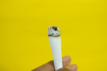 A man hand holds a handmade cigarette on yellow background