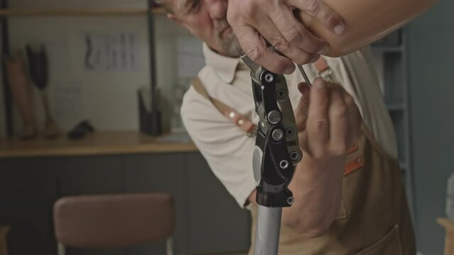 Waist up of mature Caucasian man using stainless steel allen wrench while assembling leg prosthesis in small workshop