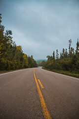 asphalt road in the fall forest with foggy hills in the background