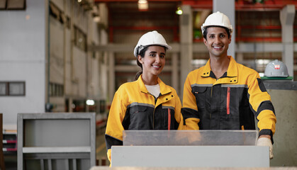 Hispanic industrial engineers in white helmet and safety jacket working in heavy metal engineering factory. Latin technician workers using tablet computer in metalwork manufacturing facility, portrait