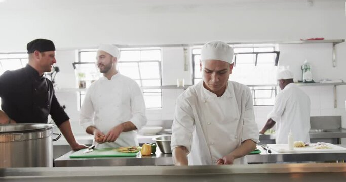 Group of focused diverse male chefs preparing meals in kitchen, slow motion