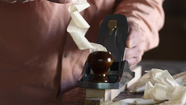 The woodworker use a hand plane and planes the workpiece, producing curly shavings and the noise of handmade work