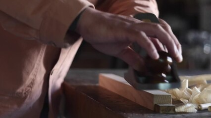 The woodworker use a hand plane and planes the workpiece, producing curly shavings and the noise of handmade work