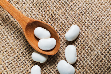 Spoon with raw organic white beans on the table and burlap sack, ingridient for healthy and nourishing legume cuisine