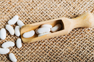 Wooden scoop with white beans on the burlap sack, goodness of legume-based nutrition.