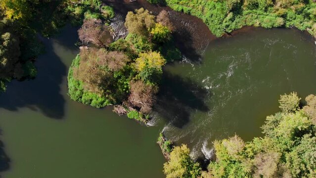 Flying along a beautiful river with rapids and curved banks. Early fall or summer. View from above vertically