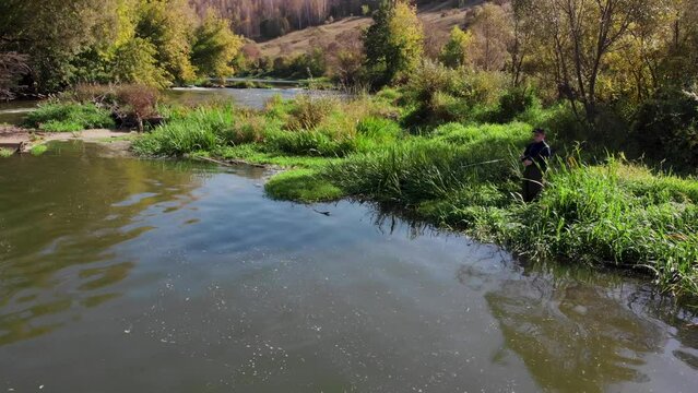 A fisherman on a river with rapids catches a spinning rod in the morning in early fall. Drone footage, fly around