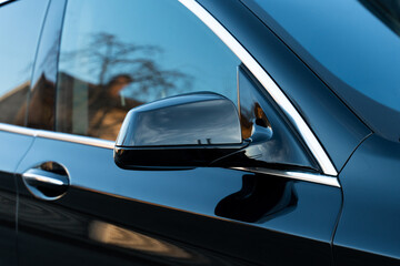 Exterior of front car door with handle, tinted glass and black side mirror. Crop of deluxe vehicle attributes