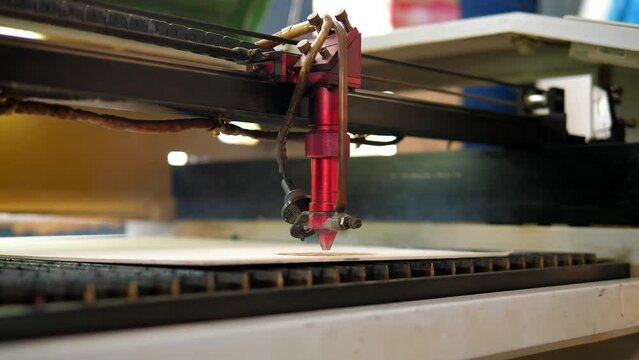 An industrial laser cuts a pattern on a sheet of plywood . Modern laser treatment of wood. A red laser beam passes through a tree.