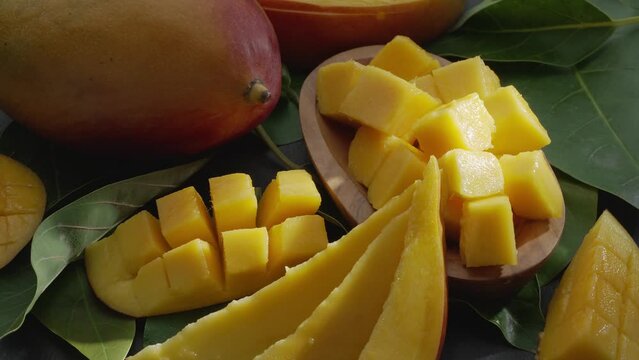 Ripe mango fruits with slices and mango leaves slowly move in the frame on a gray stone table. Nice fruit background for your projects. Macro video shooting.